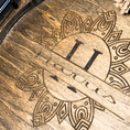 Load image into Gallery viewer, This Close-up of the Boho Bliss serving tray reveals a wooden surface with intricately carved mandala-like patterns and the word Hocus engraved. The geometric design makes this custom round tray unique and captivating.