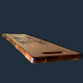 Load image into Gallery viewer, The Sophisticated Dining: Engraved Grazing Board, a long rectangular acacia wood board with a handle, elegantly rests on a dark surface, ideal for entertaining.