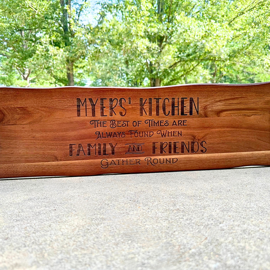 The Sophisticated Dining: Engraved Grazing Board elegantly displays MYERS KITCHEN The best of times are always found when family and friends gather round. Its perfect for entertaining, featuring a lush green trees backdrop in a bright outdoor setting.