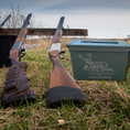 Load image into Gallery viewer, Two shotguns rest on the grass beside a Tactical Titan: Personalized Military Style Storage Can, custom-designed with a deer illustration and Craig Clouse. This storage sits by a wooden bench overlooking the water.